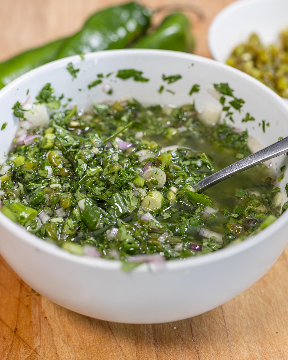 Overhead bowl of Hatch chile chimichurri with chopped shallot and scallion, whole green chiles and a shallot alongside