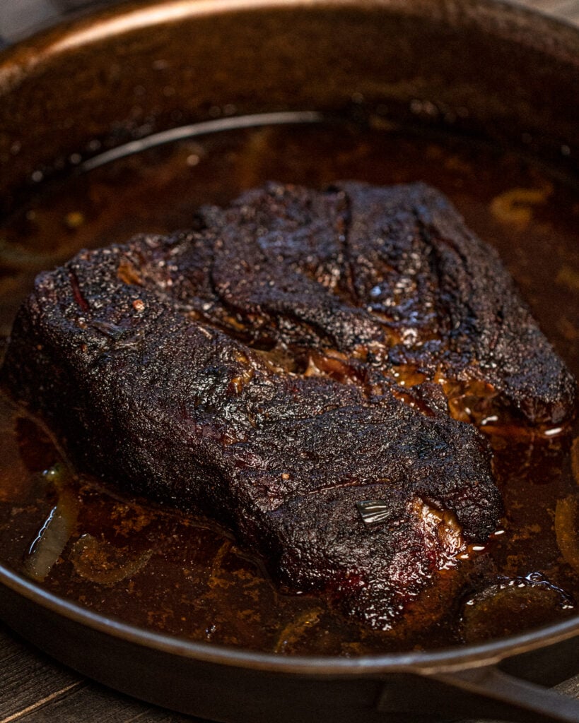 Smoked chuck roast braising in a skillet with beef broth and onions