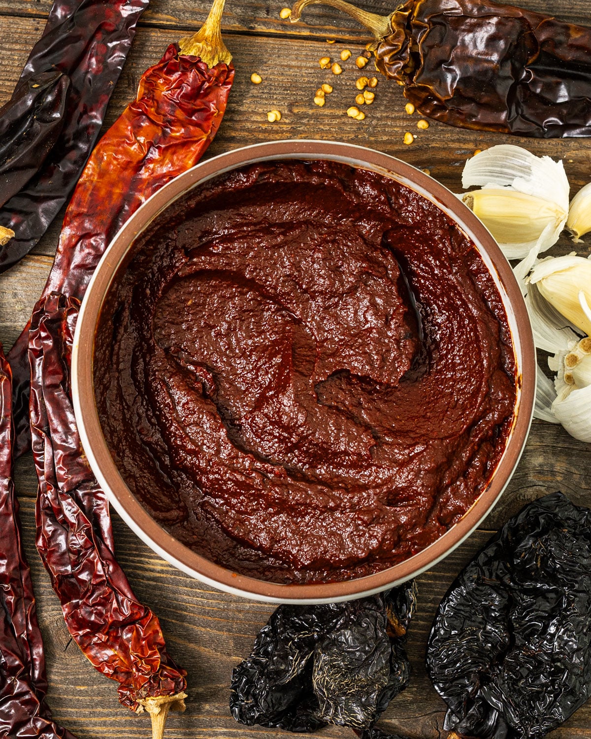 Overhead view of homemade adobo sauce made with toasted ancho and guajillo chiles, surrounded by dried chiles, garlic, and chile seeds.