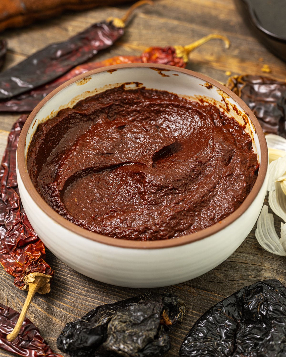 Bowl of homemade adobo sauce with dried ancho and guajillo chiles and fresh garlic on a wooden table.