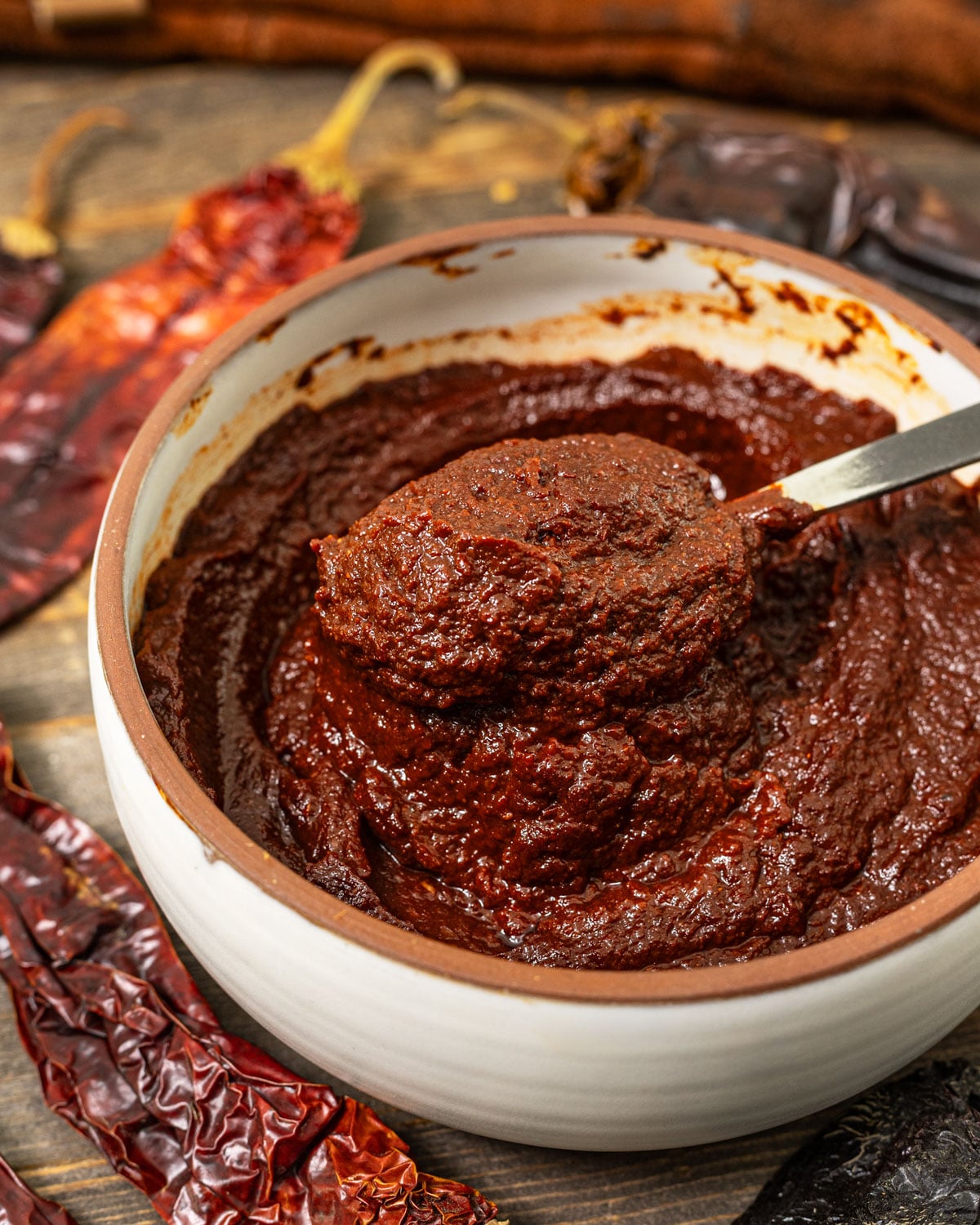 Thick homemade adobo sauce on a spoon above a bowl with dried ancho and guajillo chiles.