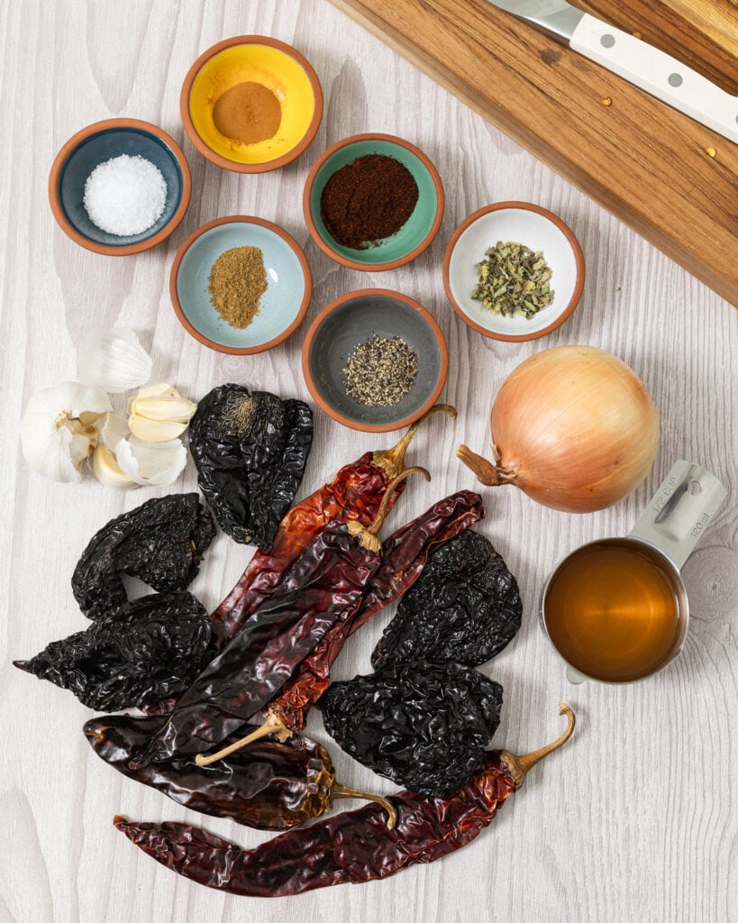 Ingredients for homemade adobo sauce including dried ancho chiles, guajillo chiles, onion, garlic, vinegar, and spices.