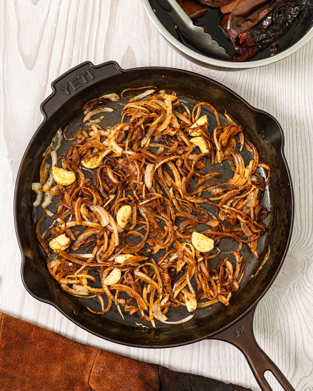 Sliced onions and garlic cooking with spices in a cast iron skillet for homemade adobo sauce.
