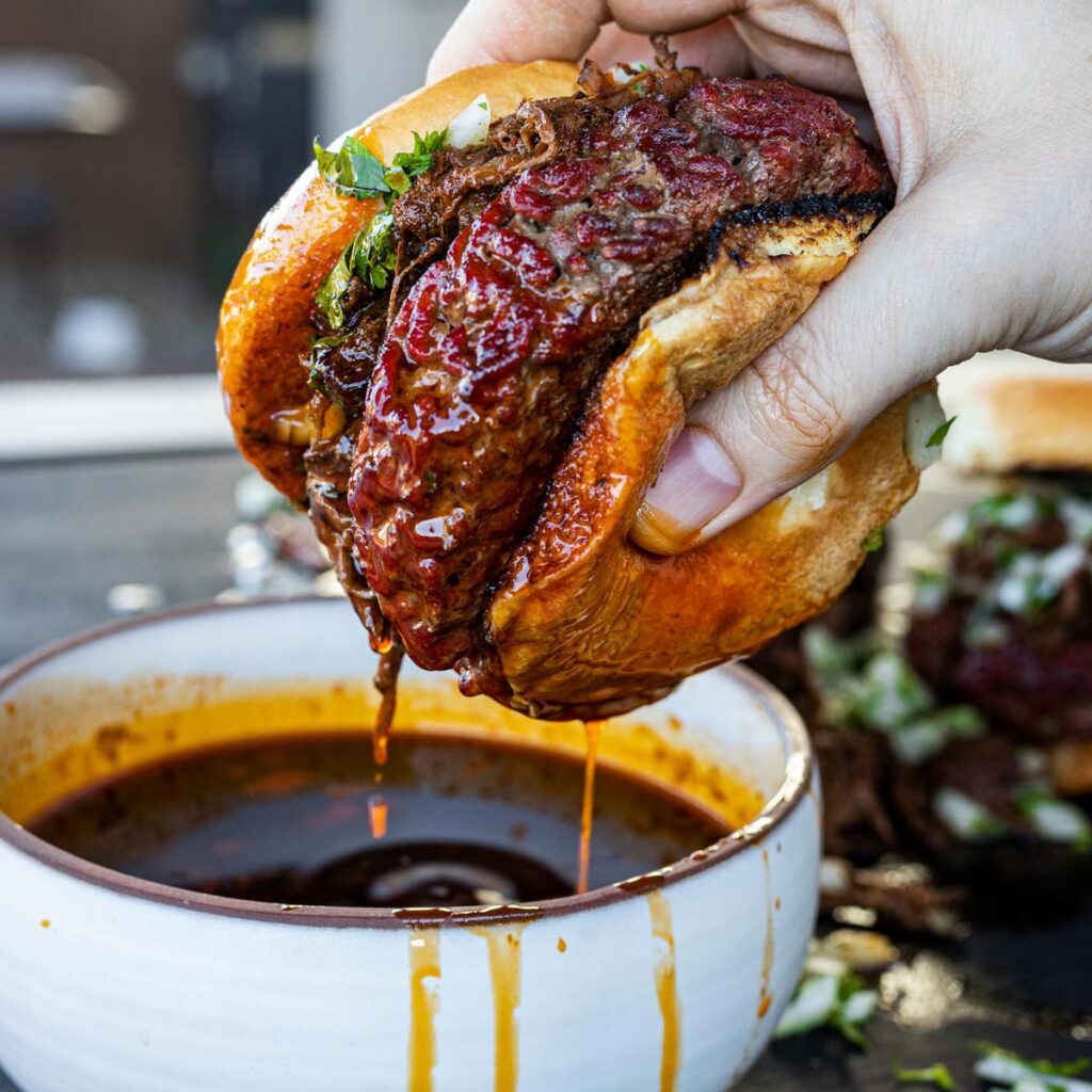 smoked beef birria burgers being dipped into consome
