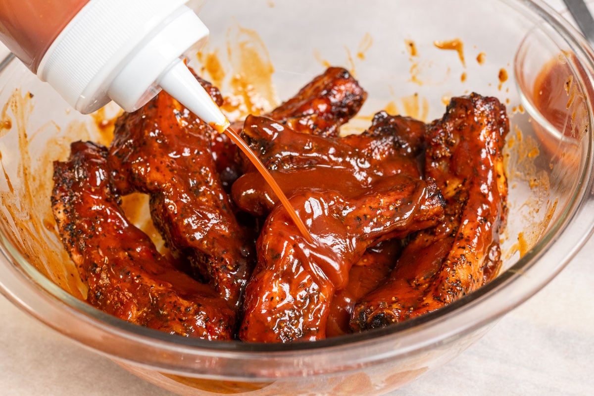 Squirting buffalo bbq sauce onto pork ribs in a bowl