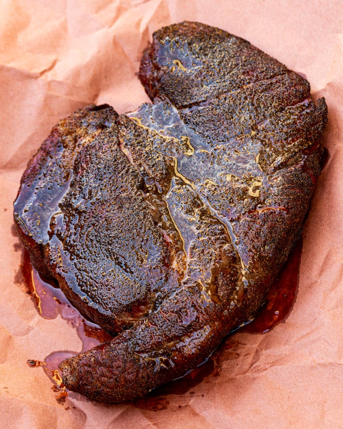 Smoked chuck roast resting on pink butcher paper after the wrap, bark glistening