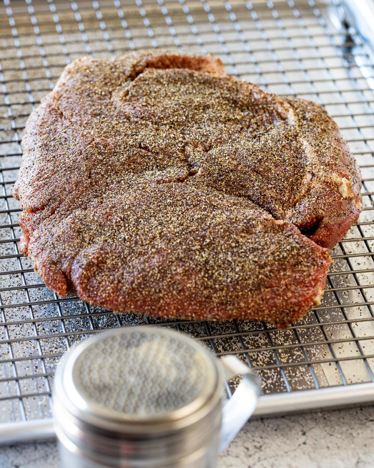 Chuck roast coated in dry rub on a wire rack before smoking