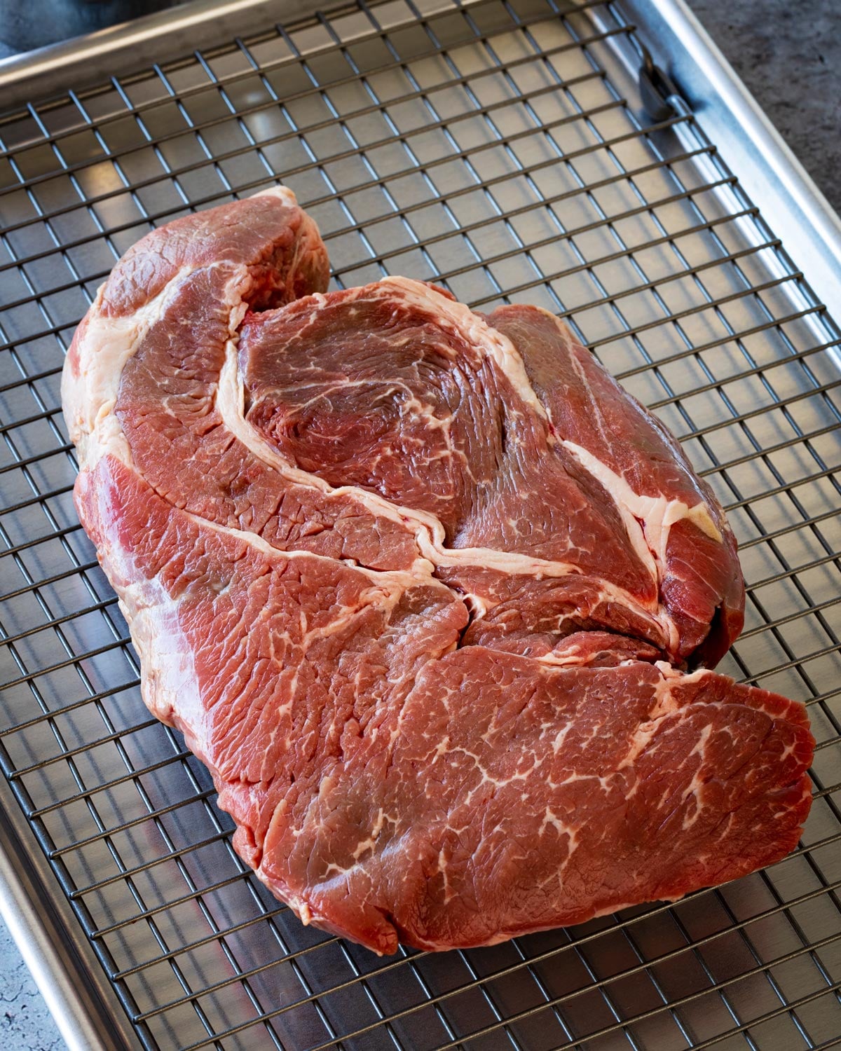 Raw chuck roast on a wire rack showing marbling and fat seam