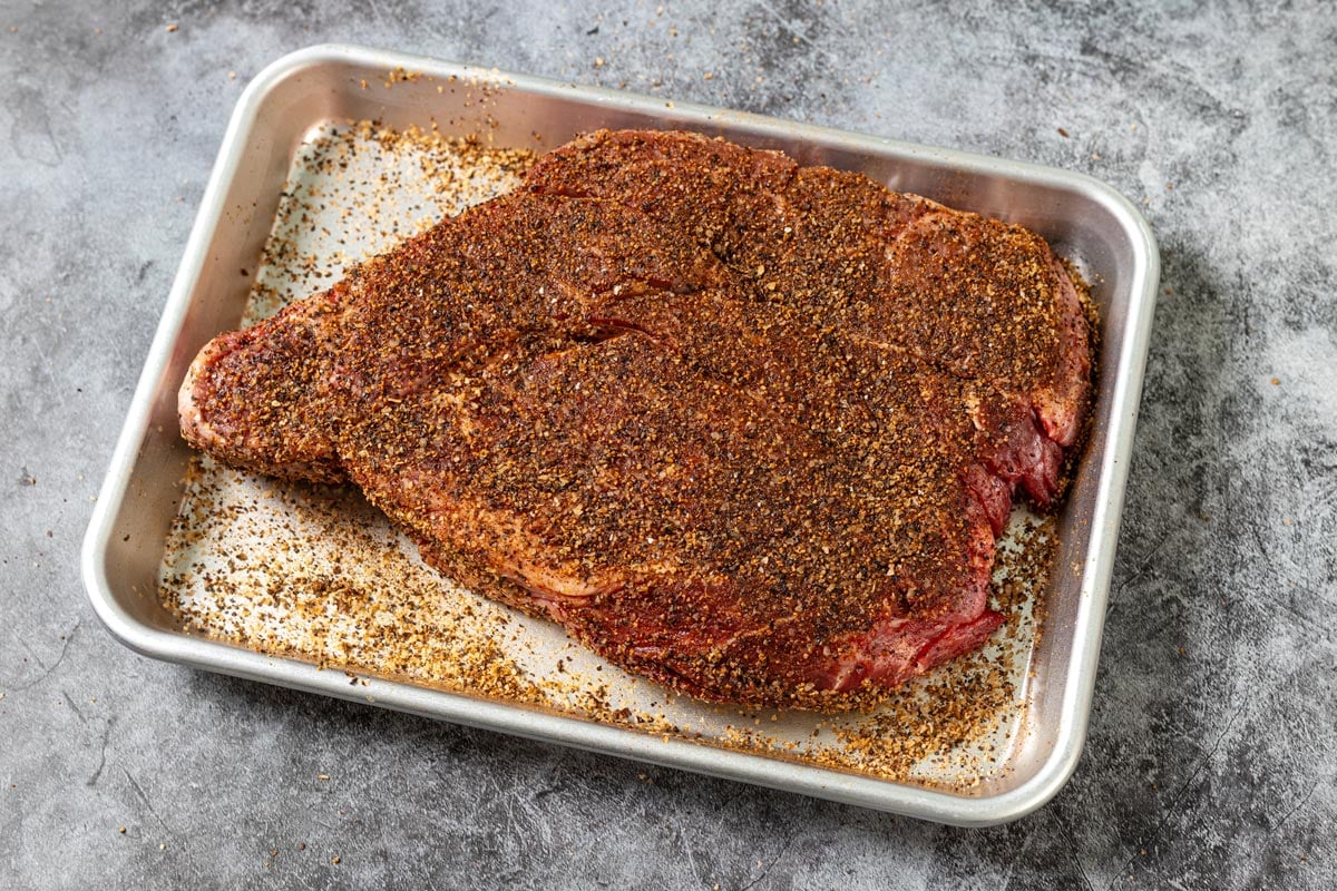 Seasoned chuck roast on a sheet pan before smoking