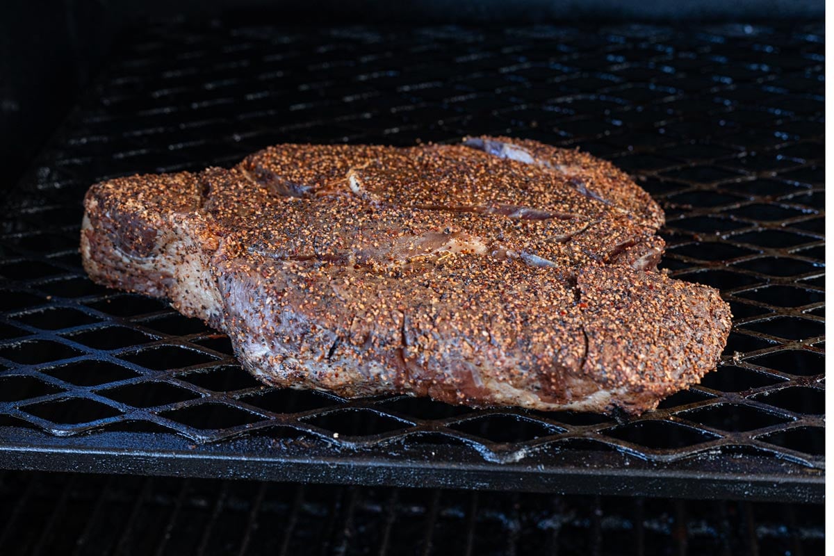 Seasoned chuck roast on smoker grates at the start of the cook