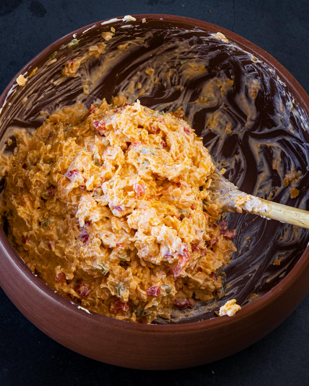 Jalapeño pimento cheese being mixed in a terracotta bowl with a wooden spoon, showing the fully combined spread