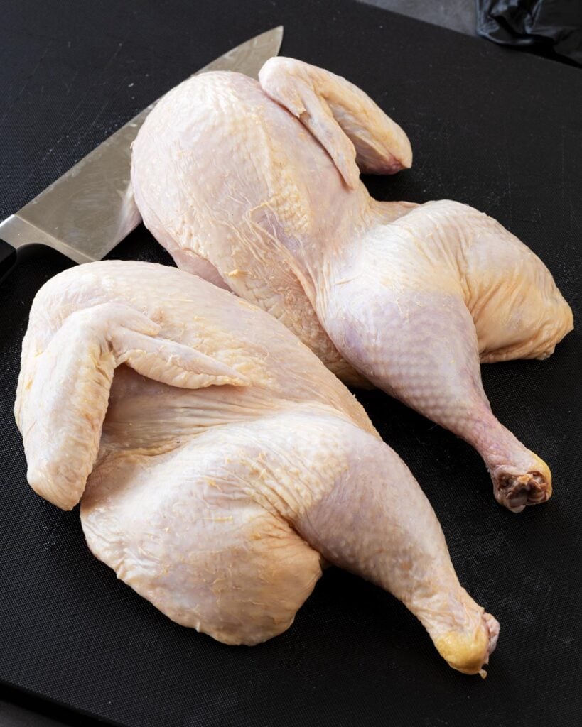 Using a chef knife to split the chicken into two halves.