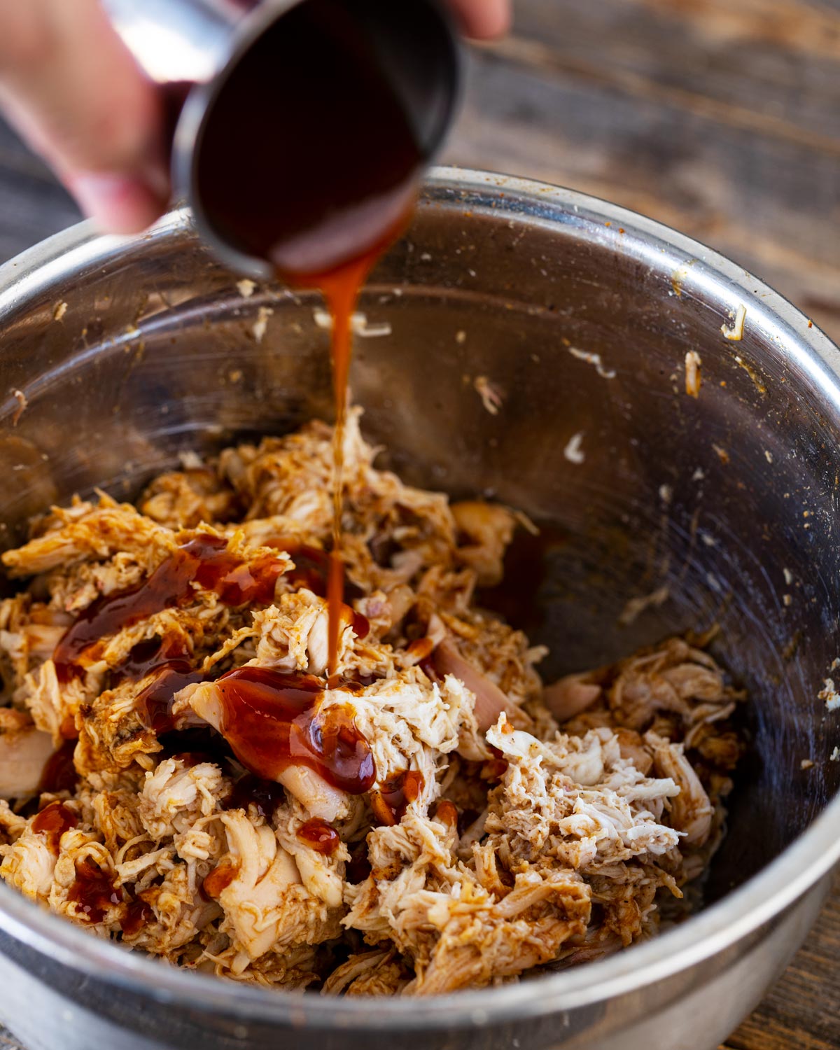 Pouring warmed bbq sauce into the shredded chicken.
