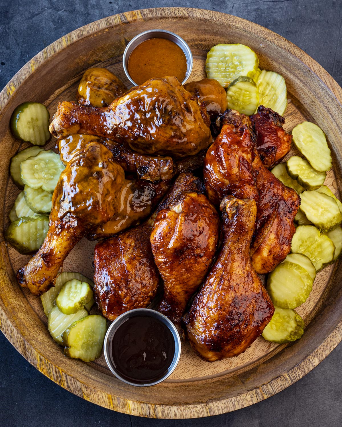 Wooden platter of pickles, sauces, and smoked chicken legs.