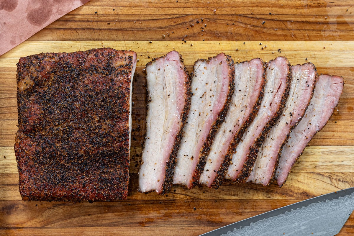 Texas-style smoked pork belly slab and slices on a cutting board, overhead view showing bark and smoke ring