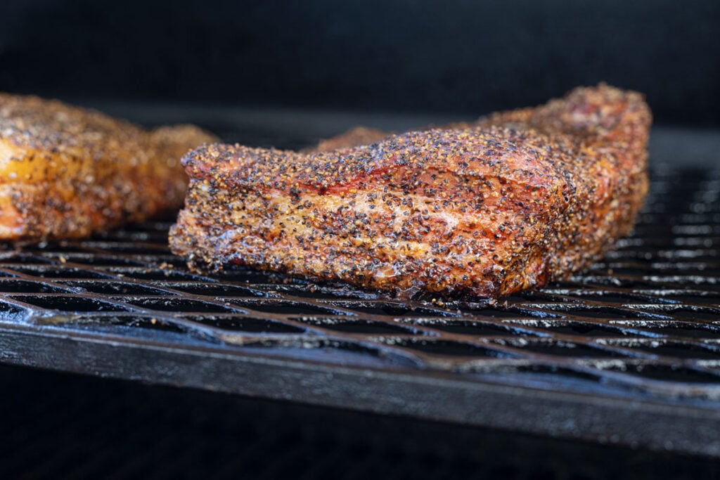 Smoked pork belly slab on smoker grates with bark forming and fat beginning to render