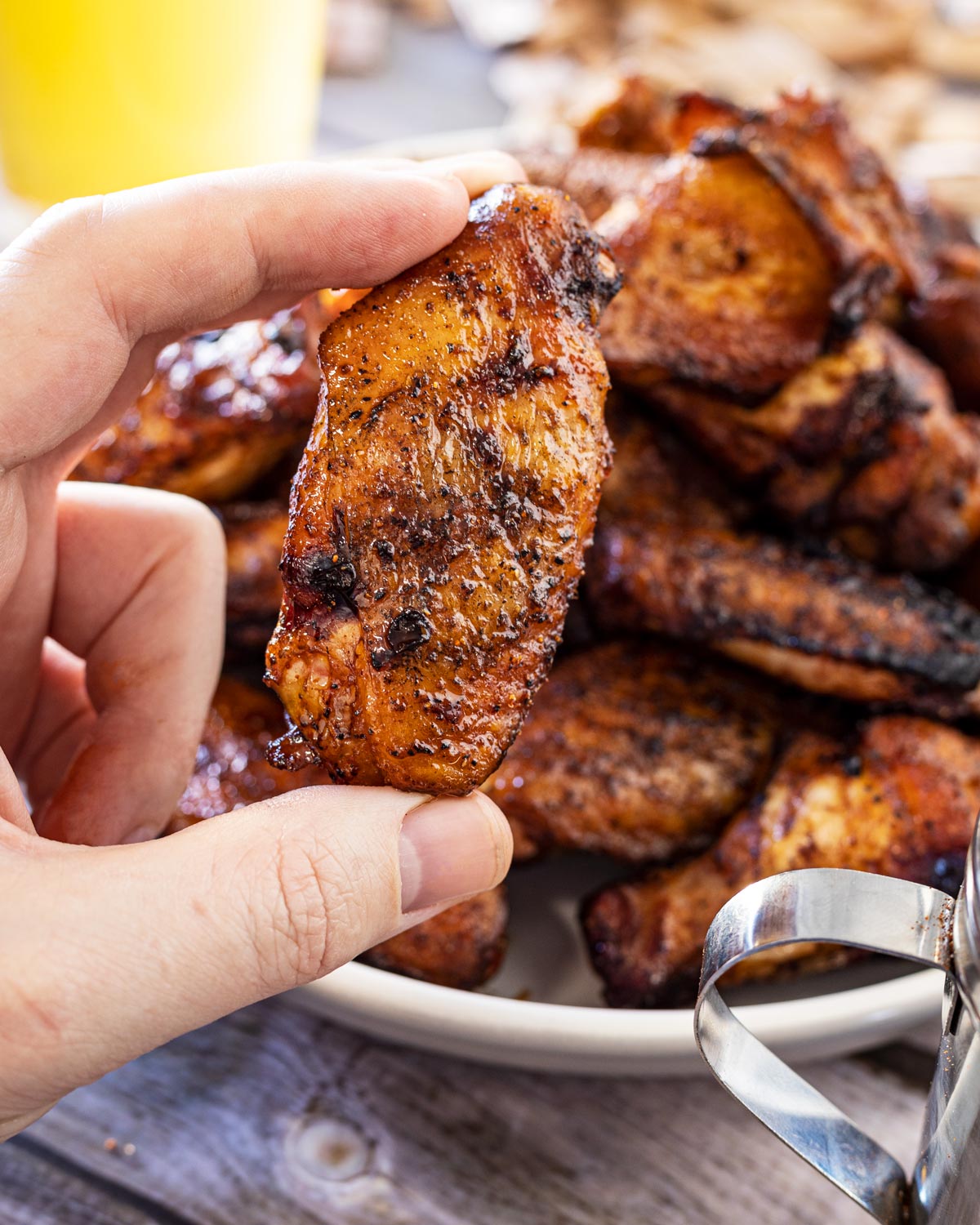 Hand holding a single grilled chicken wing with charred, crispy skin