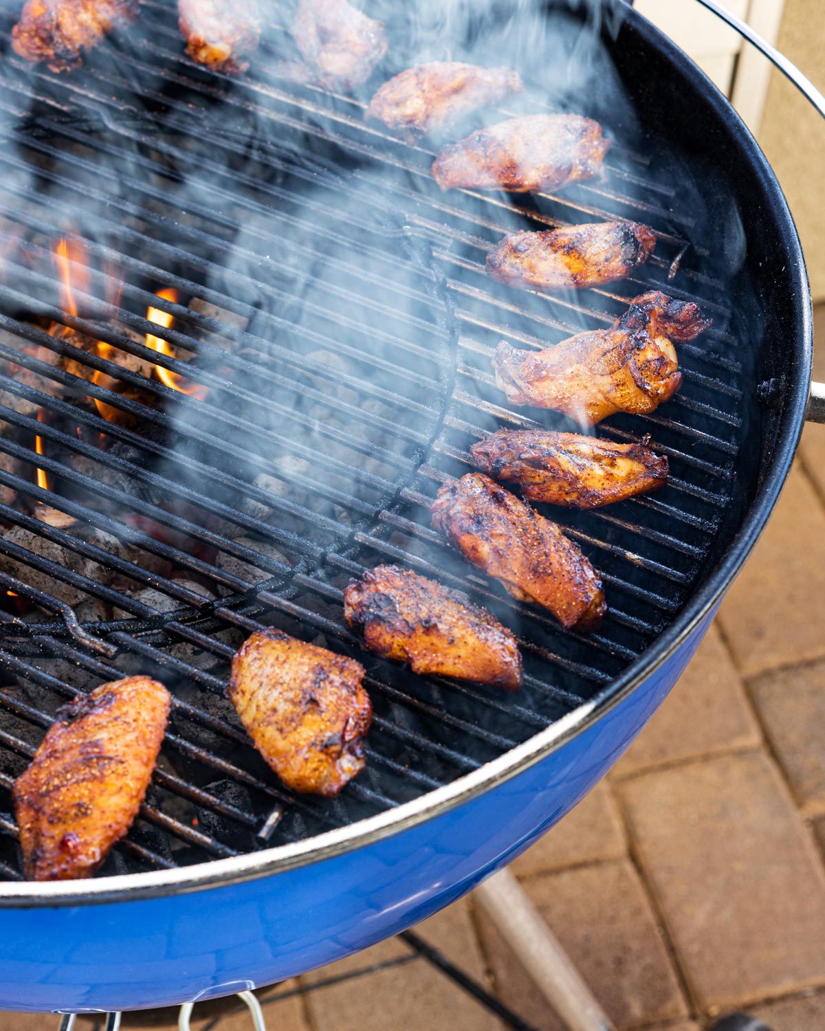 Chicken wings cooking on the indirect side of a charcoal kettle grill with smoke rising