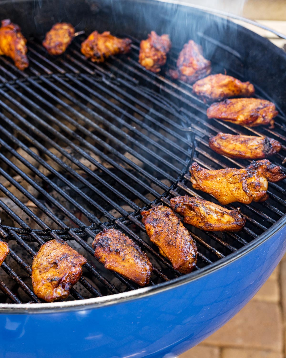 Seasoned chicken wings arranged on the cool side of a two-zone charcoal grill with smoke