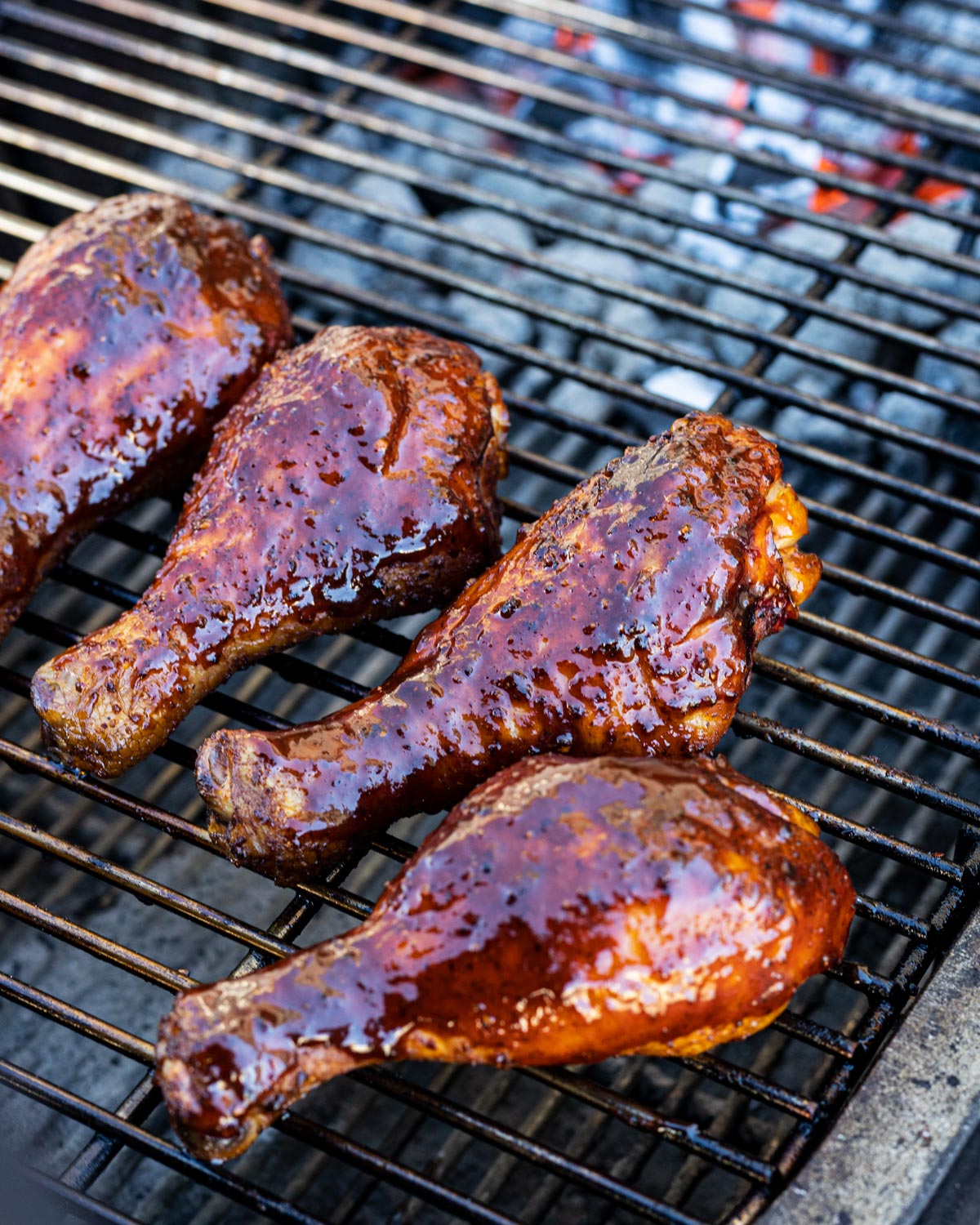 Korean BBQ glazed chicken drumsticks cooking on a charcoal grill grate over coals