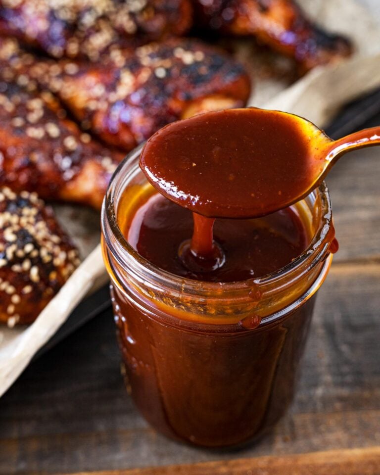 Thick Korean BBQ sauce dripping off a spoon into a glass jar, glazed drumsticks behind