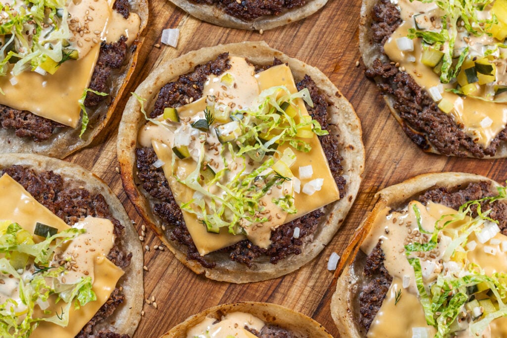 Big Mac smash burger tacos with crispy beef, American cheese, burger sauce, shredded lettuce, pickles, and sesame seeds on a wood board — Chiles and Smoke