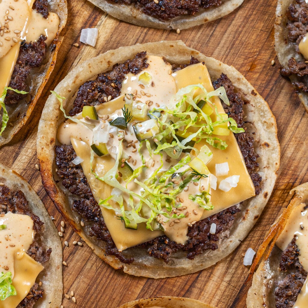 The original smash burger taco with crispy beef crust, American cheese, burger sauce, shredded lettuce, pickles, and sesame seeds on a flour tortilla — Chiles and Smoke