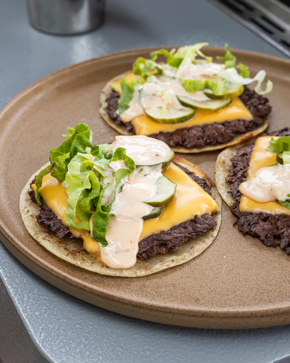 Smash burger tacos with pickles, lettuce, and burger sauce on a brown plate.
