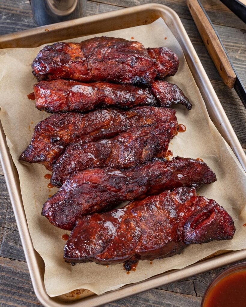 Smoked country style ribs glazed with BBQ sauce on a parchment-lined sheet pan