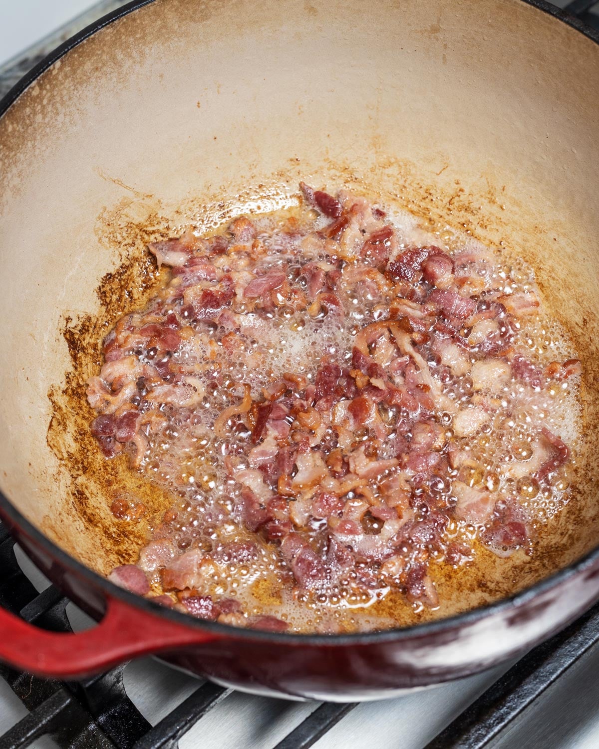 Diced thick-cut bacon rendering in a red Dutch oven on the stovetop