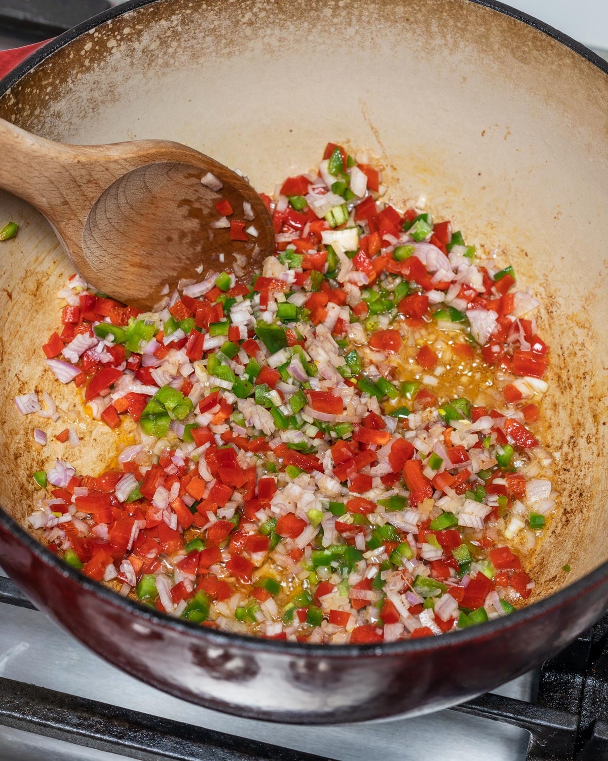 Diced red bell pepper, jalapeno, and shallots sauteing in bacon fat in a red Dutch oven