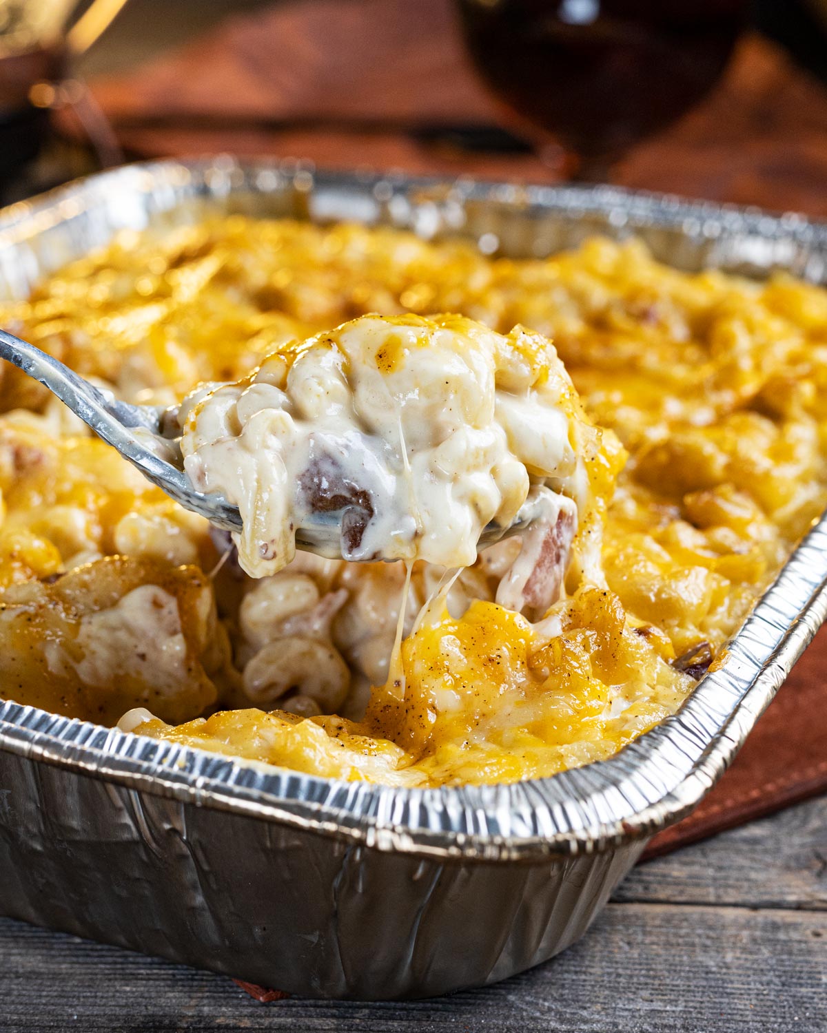 Creamy smoked mac n cheese with bacon in a foil pan with a spoonful.