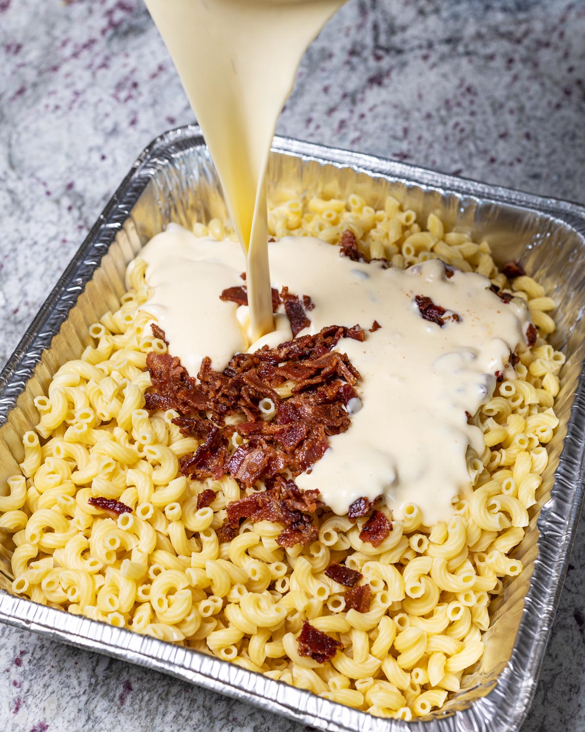 Add the macaroni to a foil pan with bacon, and pour in the cheesy sauce.