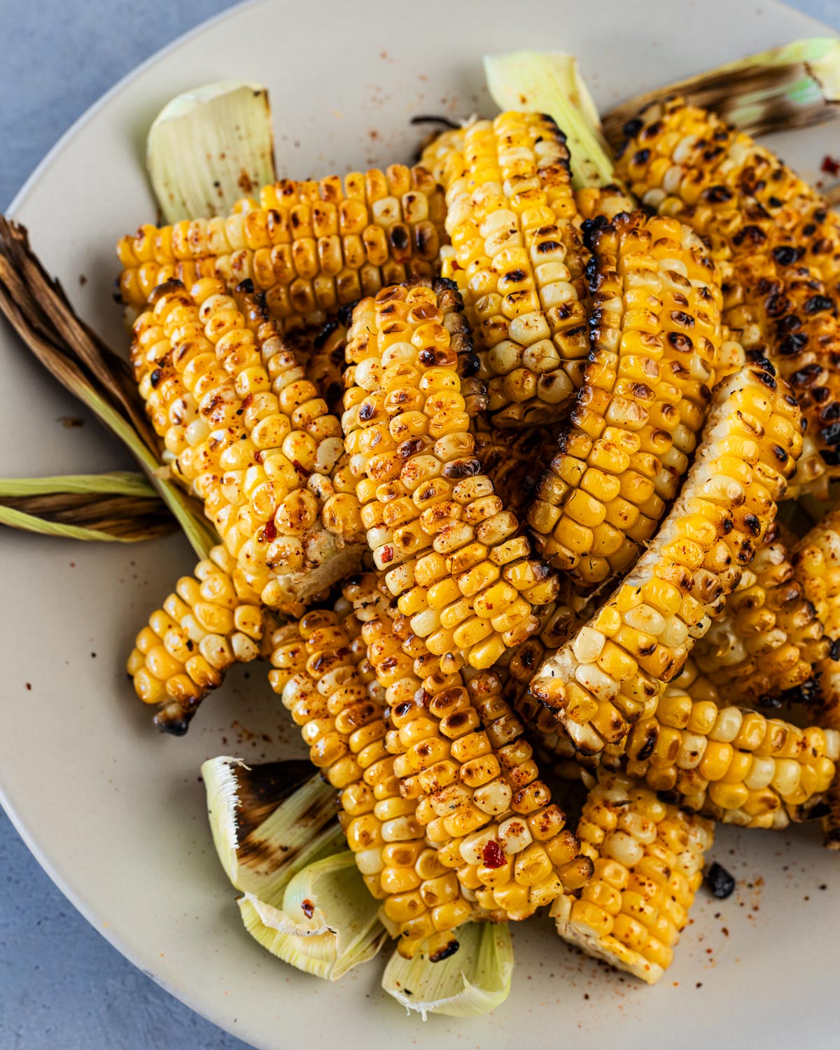 Grilled corn ribs piled on a plate with charred kernels and chile seasoning, corn husks tucked underneath