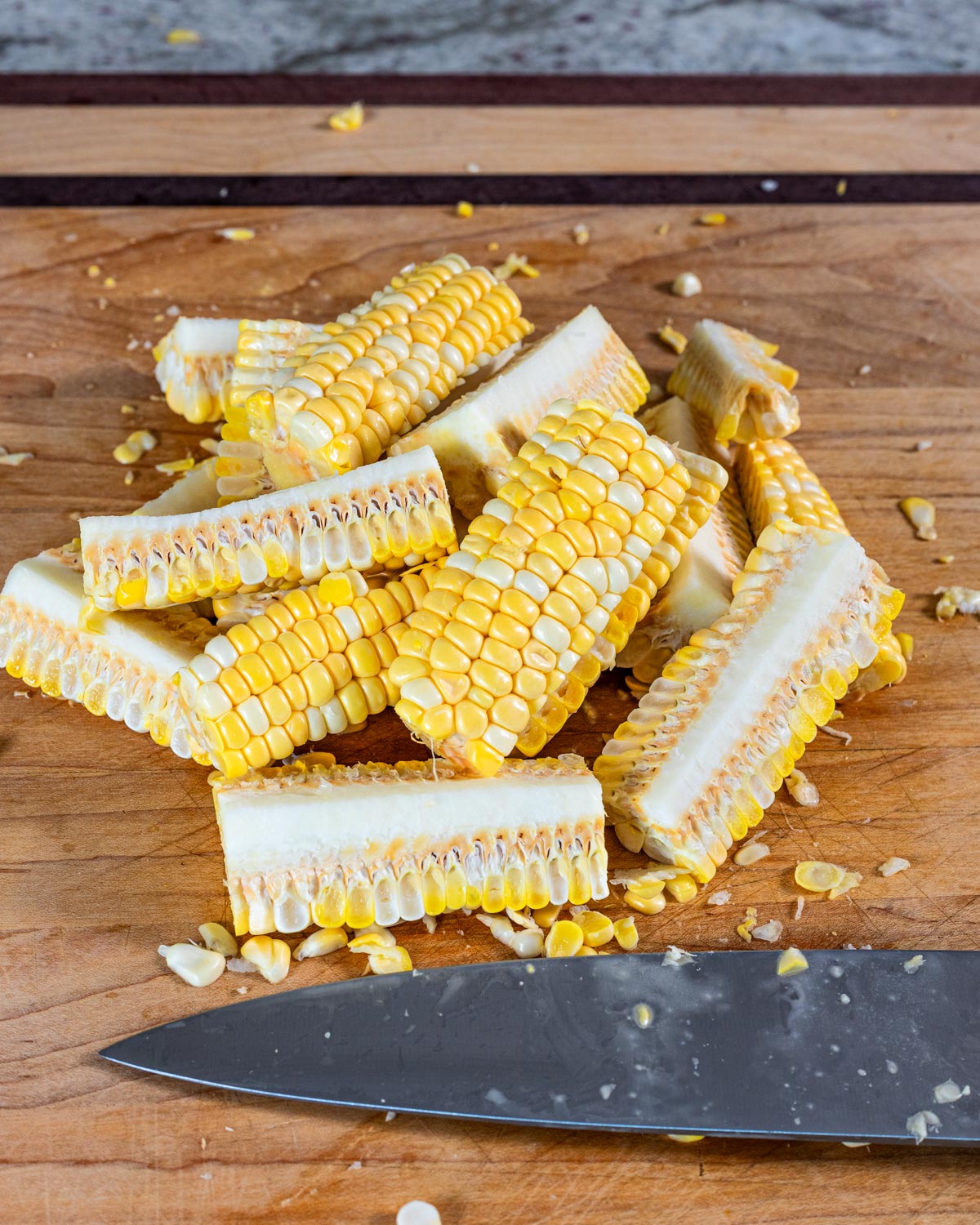 Fresh corn ribs quartered and ready to grill on a cutting board with a knife alongside