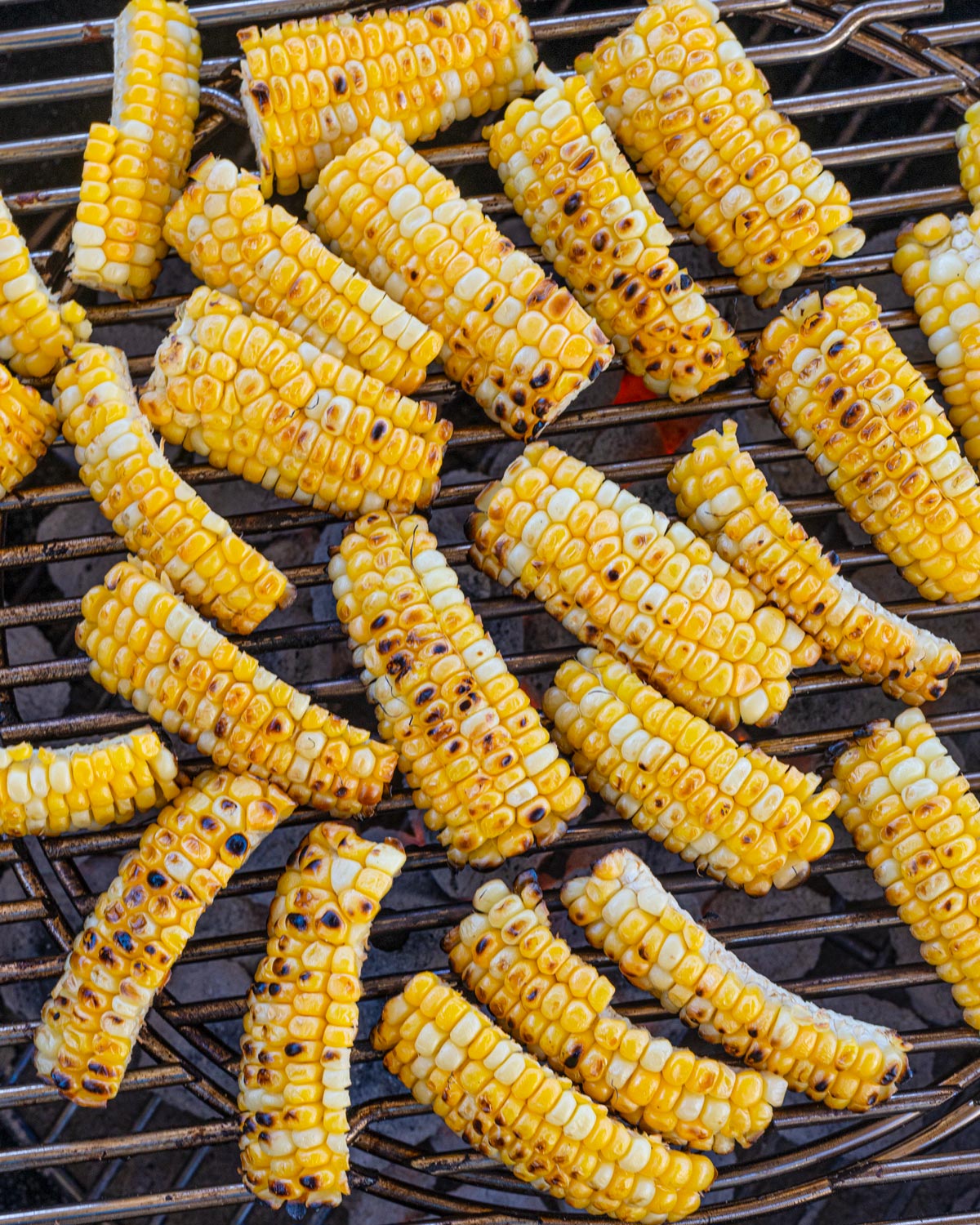Grilled corn ribs charred and curling on charcoal grill grates over live fire