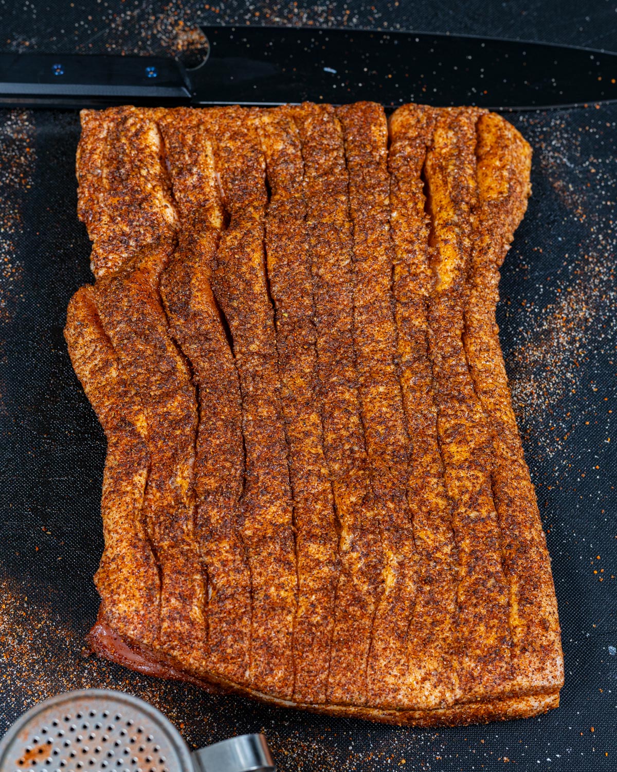 Pork belly slab generously coated in Sedona Sand rub with seasoning visible deep into the scored cuts
