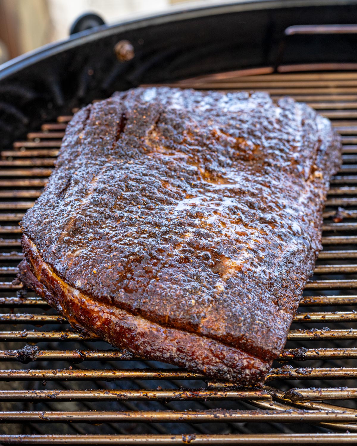 Smoked pork belly slab with dark bark and rendered fat resting on a charcoal grill grate
