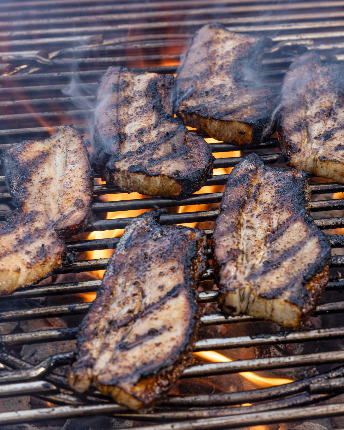 Pork belly strips searing over direct charcoal flames on a kettle grill