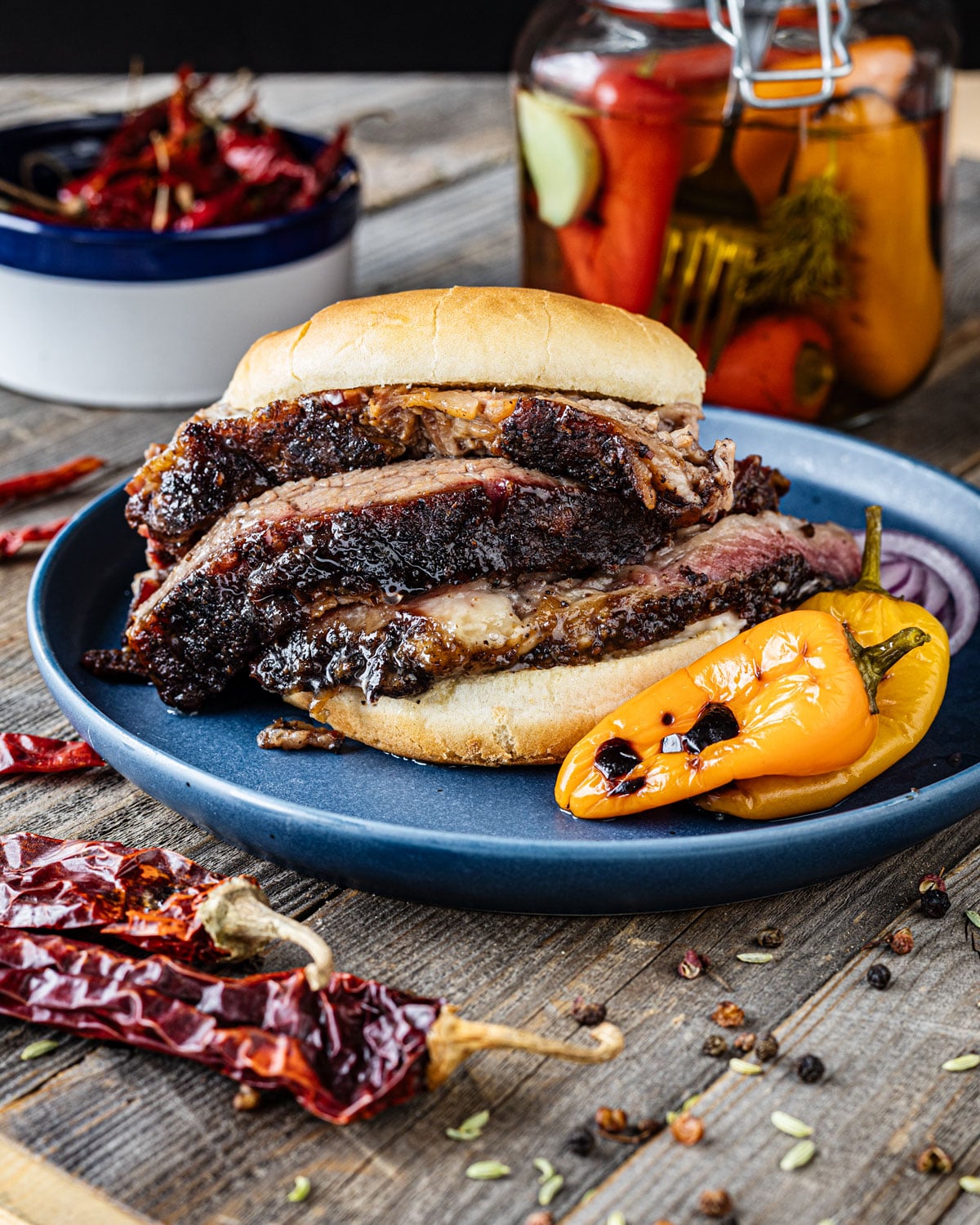 Smoked brisket sandwich on a blue plate with charred pepper and dried chiles showing bark on sliced brisket