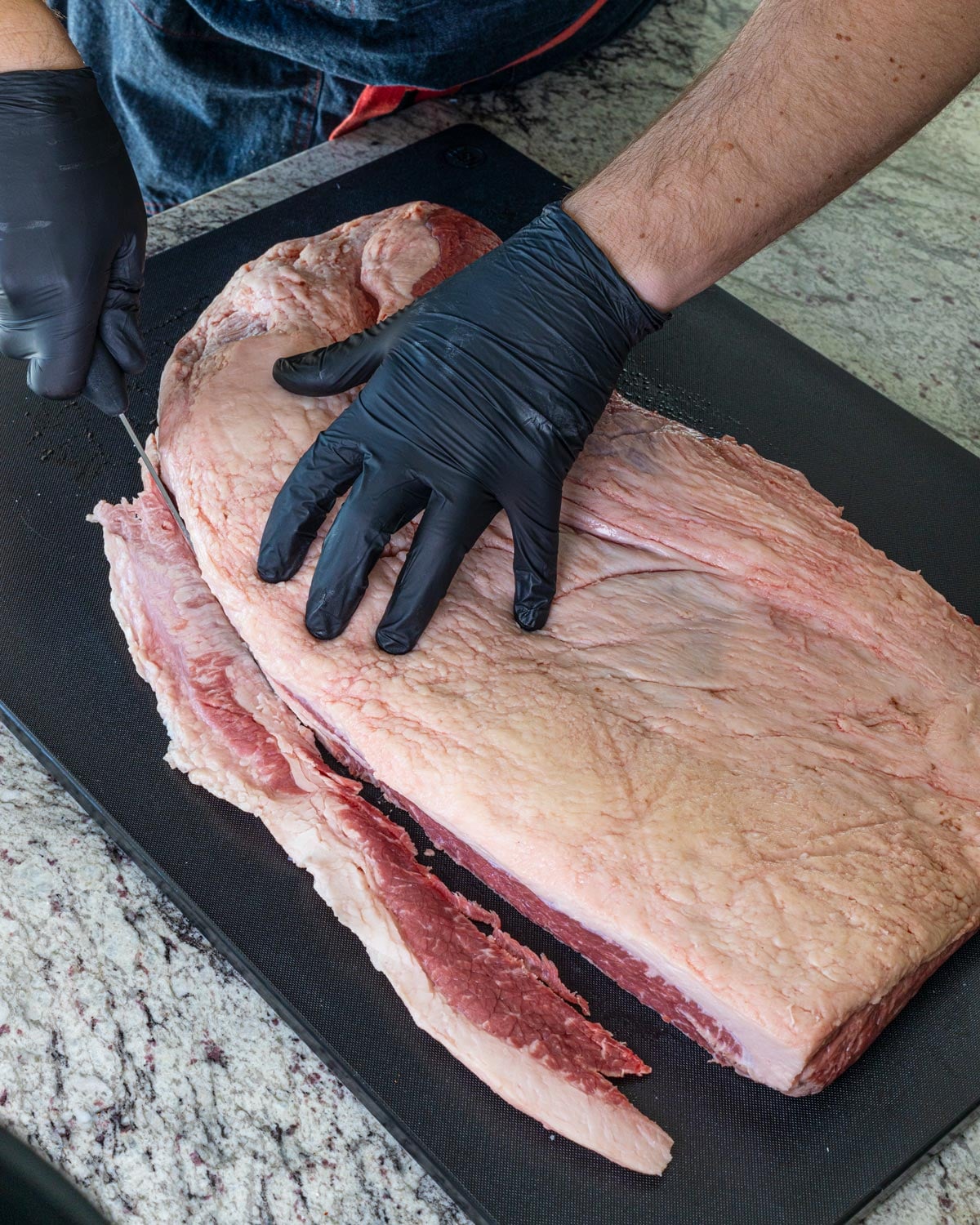 Trimming the fat cap on a raw whole packer brisket with a boning knife leaving a quarter inch