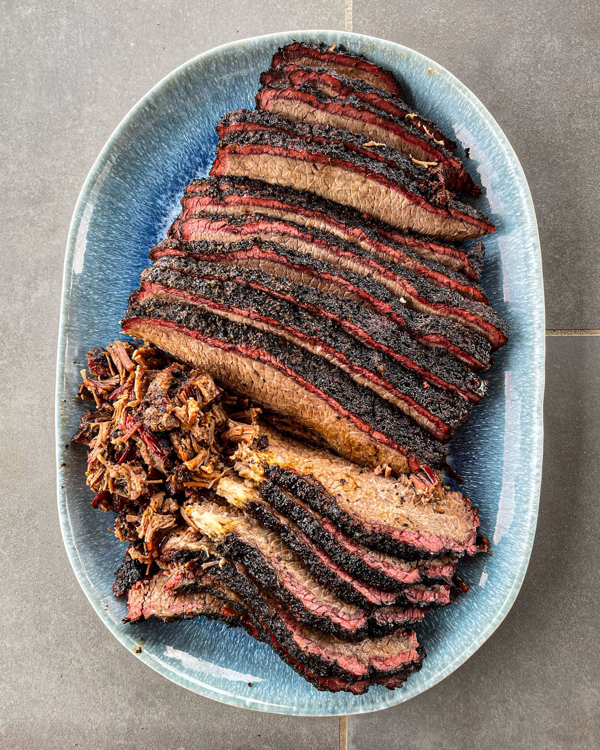 Sliced smoked brisket flat and pulled point served on a blue ceramic platter showing smoke ring and dark bark