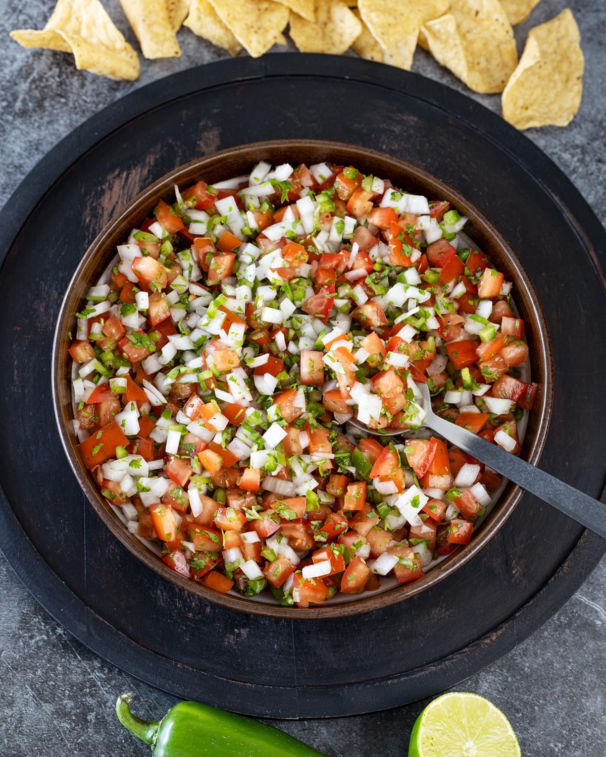 fresh pico de gallo in a wooden bowl with a spoon, tortilla chips scattered around