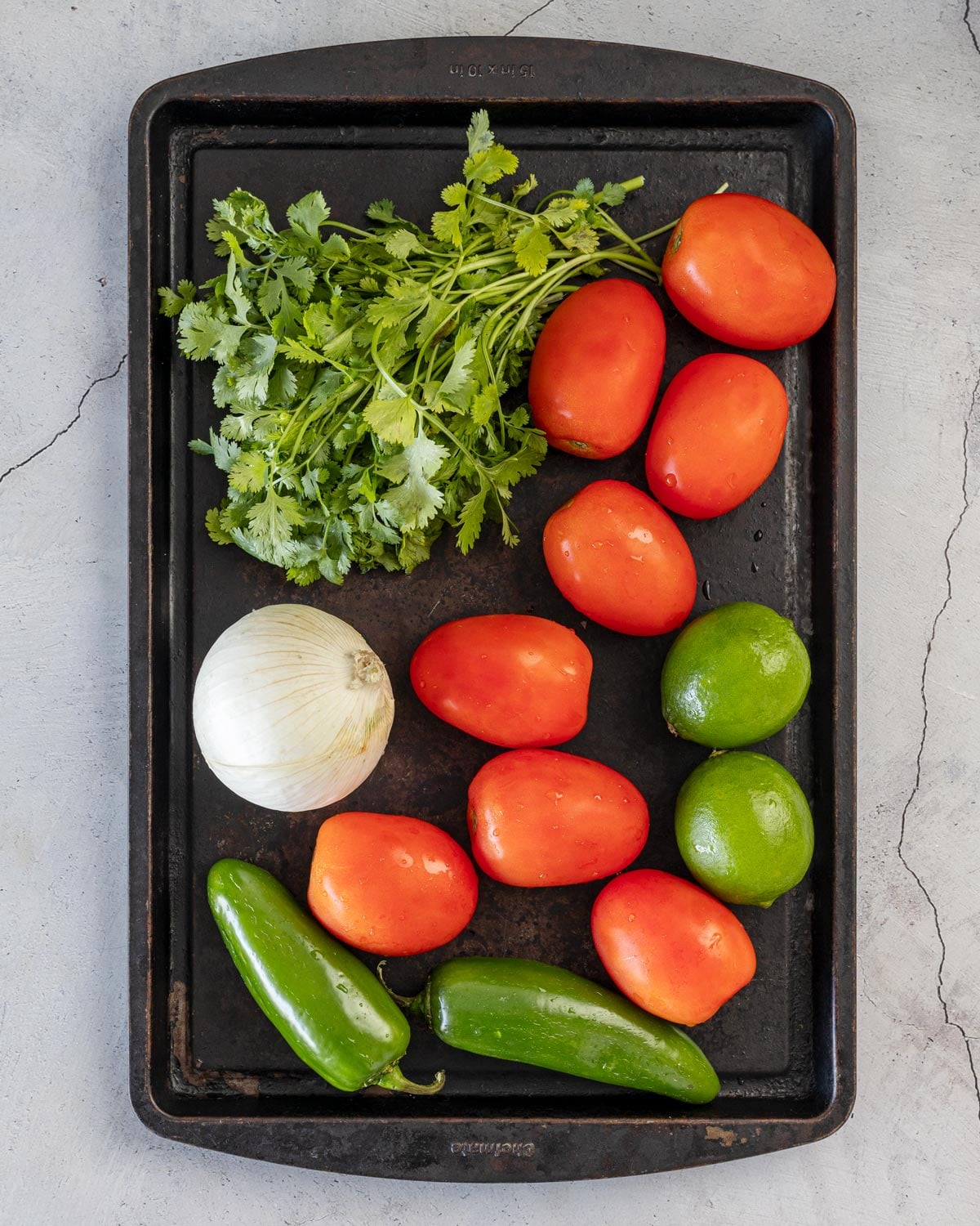 Roma tomatoes, white onion, jalapeños, limes, and cilantro on a sheet pan