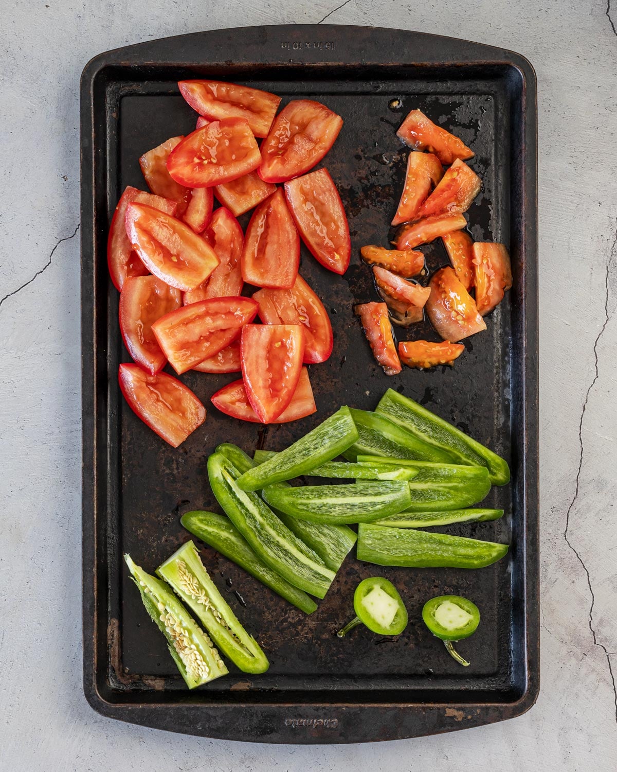 Roma tomatoes quartered and seeded with jalapeños split and deribbed on a sheet pan