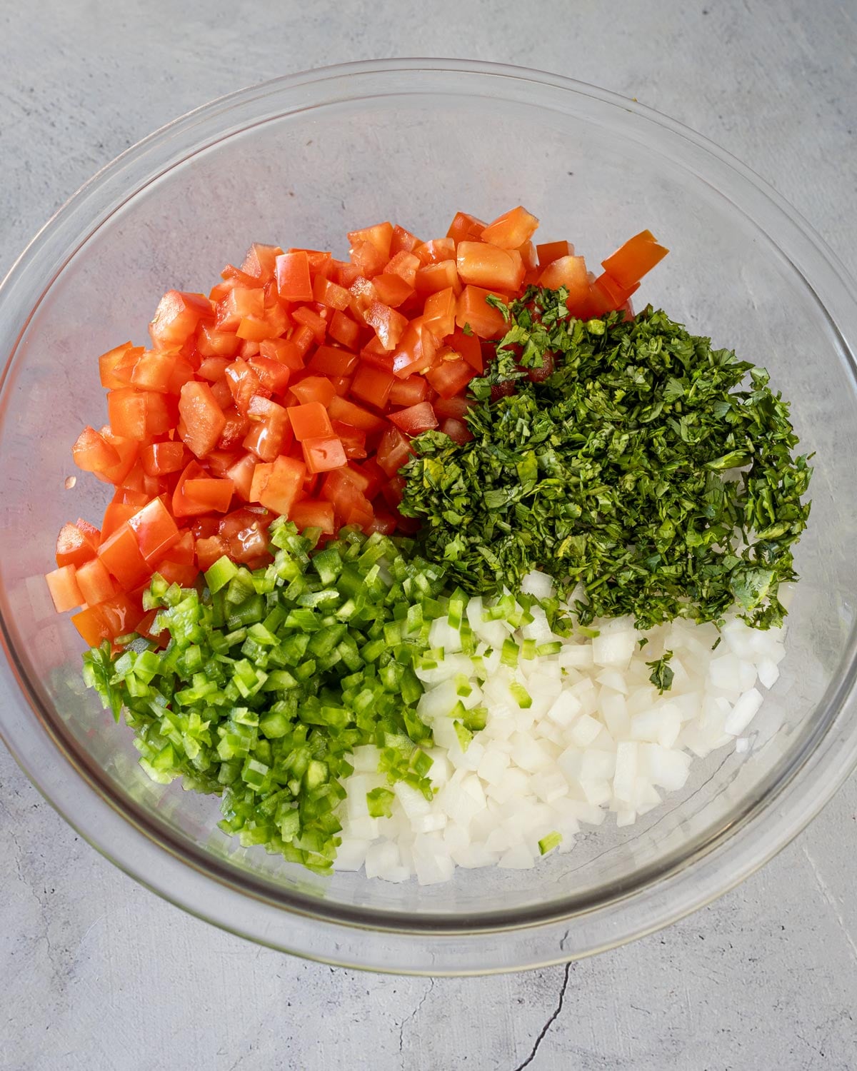 diced Roma tomatoes, white onion, jalapeño, and cilantro in a glass bowl before mixing