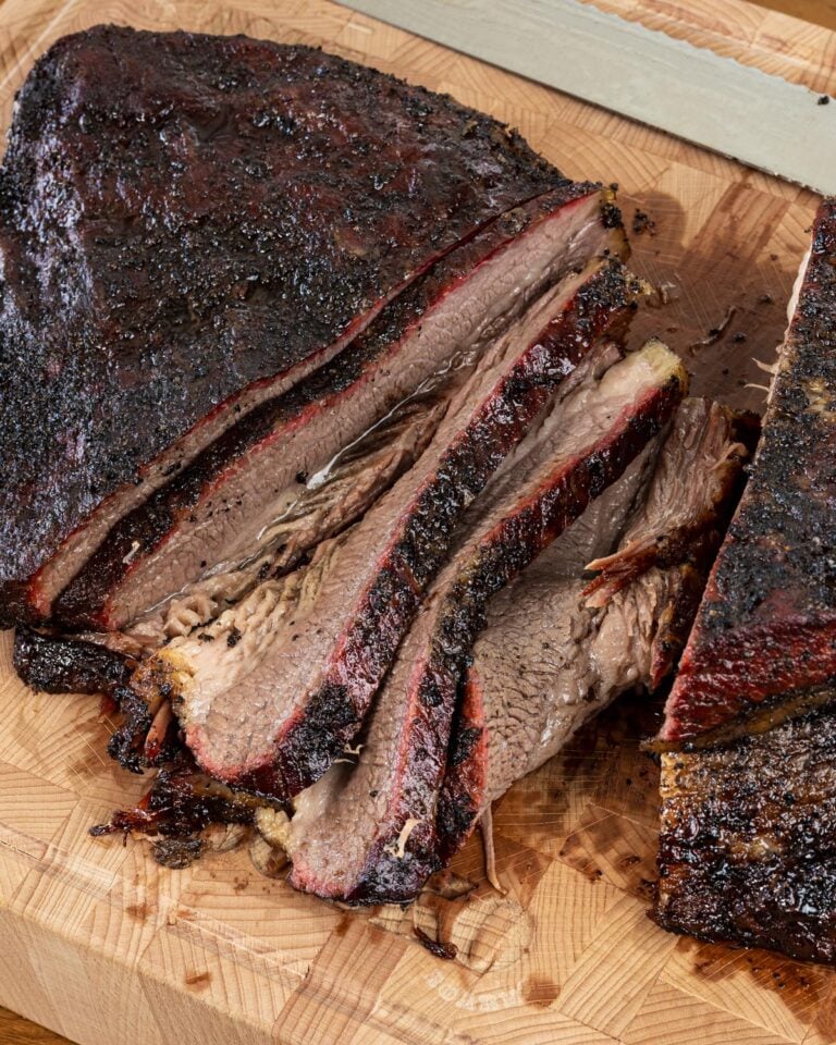 Texas-style smoked brisket sliced against the grain on a butcher block showing deep smoke ring and dark bark