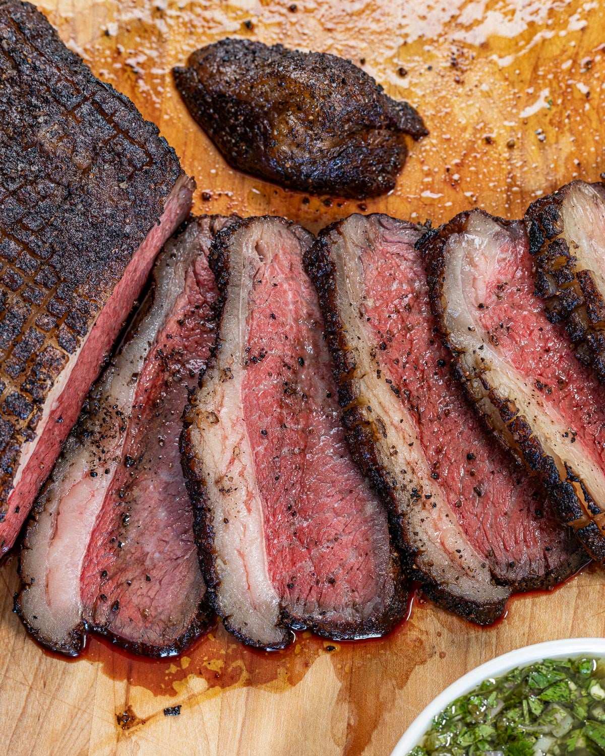 Overhead view of sliced reverse-seared picanha on a cutting board with chimichurri