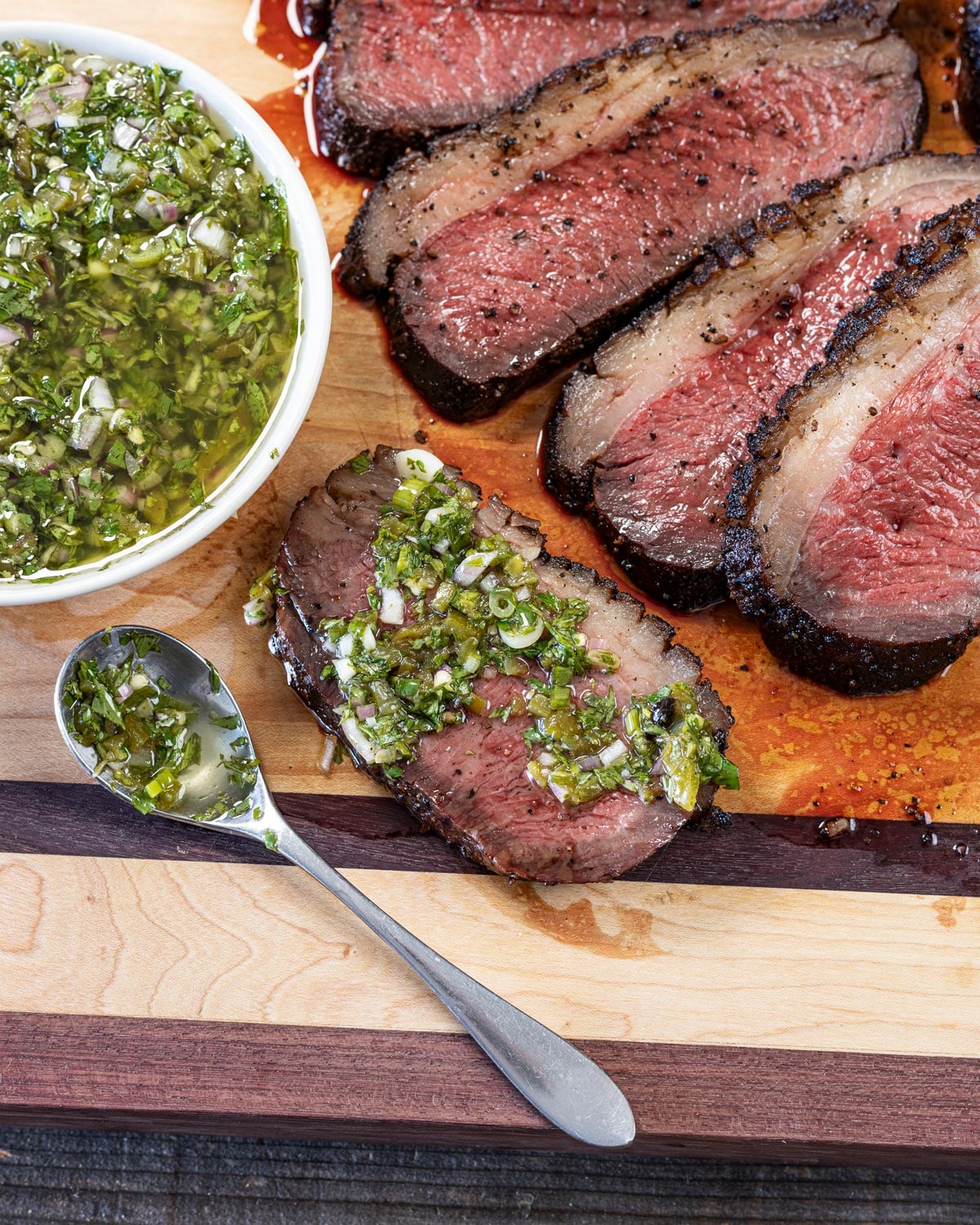 Overhead view of sliced reverse-seared picanha on a cutting board with chimichurri