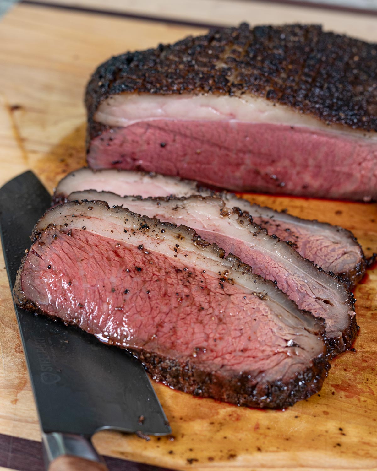 Sliced reverse-seared picanha on a cutting board showing pink interior, rendered fat cap, and dark bark